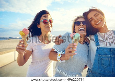 Laughing teenage girls eating ice cream cones as they walk along a beachfront promenade arm in arm enjoying their summer vacation Royalty-Free Stock Photo #496220794