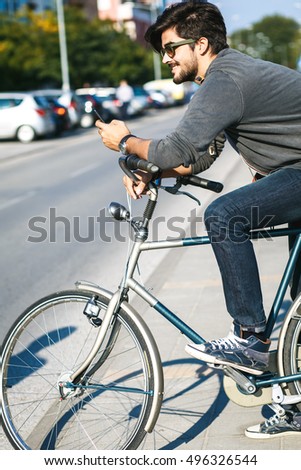 Young handsome guy with a bicycle on street, he is holding mobile phone.