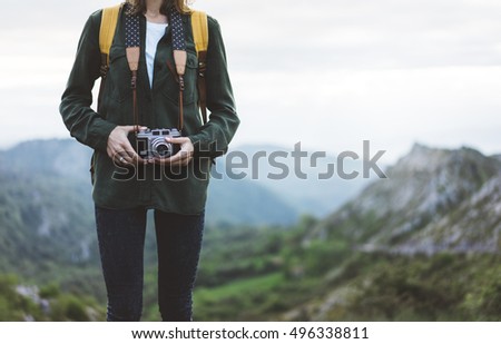 Hipster girl with backpack enjoying sunset on peak of foggy mountain, tourist traveler taking pictures of amazing landscape on vintage photo digital camera on background valley view mockup sun flare