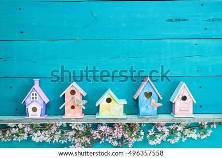 Blank sign with colorful birdhouses with butterfly on shelf by spring tree flowers on antique rustic wood background; pink, yellow, purple, orange birdhouses with teal blue copy space