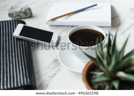 coffee, phone and empty notepad with pencil on marble background. On a first plan plant in pot out of focus
