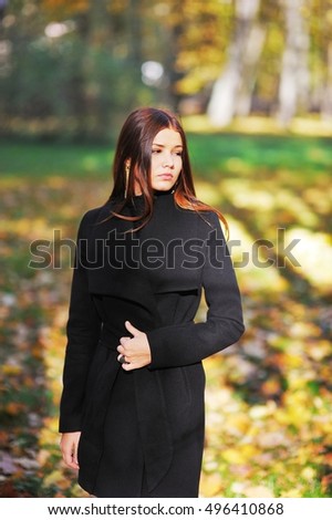 Magnificent portrait of a pensive girl with a bright-brown hair in black coat warm sunny day in autumn park.