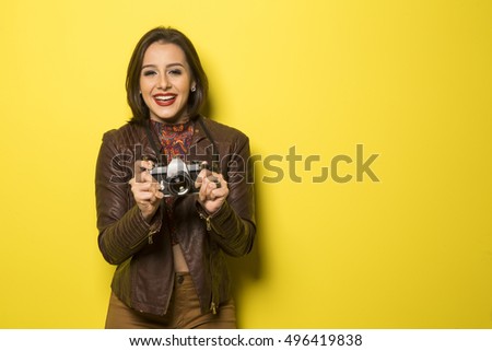 Fashion young girl makes the photo with old camera. Yellow background