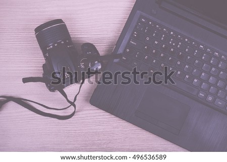 Lay flat image of a laptop and camera on a wooden surface Vintage Retro Filter.