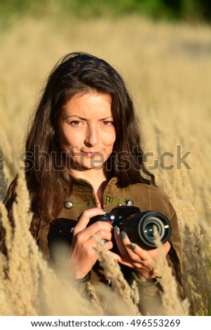 Portrait of young, long haired brunette girl, nature photographer in tall, golden colored grass in the middle of autumn field, ready in position for nice nature photos