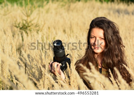 Portrait of young, long haired brunette girl, nature photographer in tall, golden colored grass in the middle of autumn field in afternoon sunlight