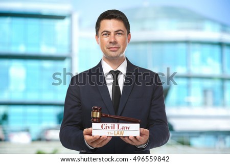 Handsome man with law books and judge gavel on blurred building background. Justice concept.