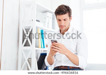 Young businessman sitting on the table and using smartphone in office