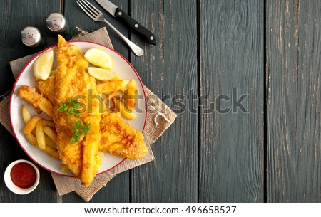 Two pieces of battered fish on a plate with chips on a wooden table with space  Royalty-Free Stock Photo #496658527