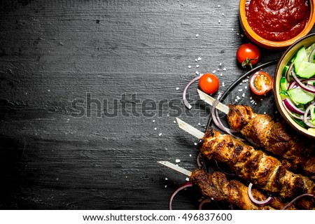 Shish kebab of pork and salad. On the black wooden table. Royalty-Free Stock Photo #496837600