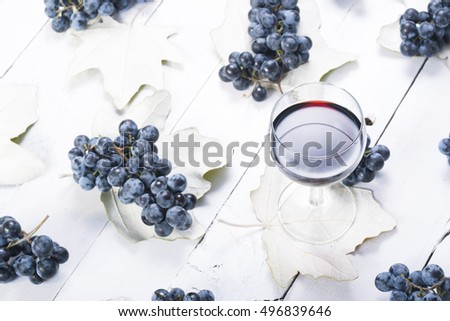 glass of red wine, blue grapes and leaves on white wooden table background