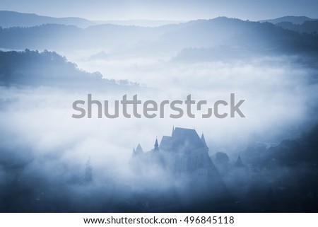 Mysterious misty morning over Biertan village, Transylvania, Romania. Blue colors. spooky, Halloween concept