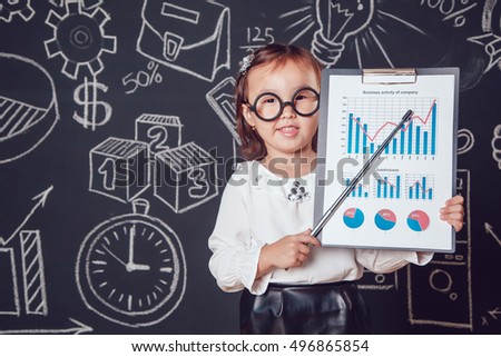 The little smart girl in glasses shows graphics company's activity on a background of wall with business or school picture