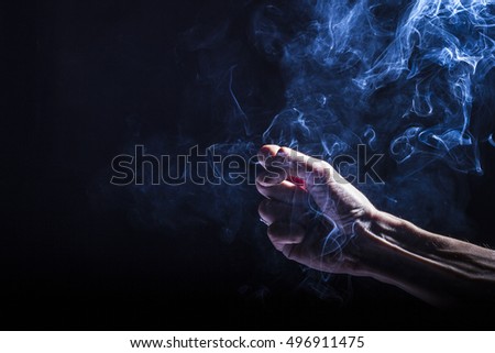 Man's hand holding and playing with smoke, dramatic and dark, black background. Smoke bender, elemental control