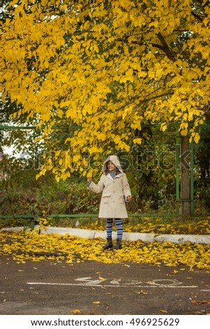 brunette girl in a light coat with a hood in yellow autumn leaves