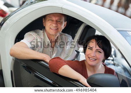 Portrait of smiling mature man and woman standing near twizy electric outdoors