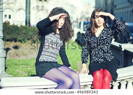 Two teenage sisters were sitting on the street and watch something a shade the eyes from the sun, which is on their eyes