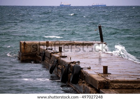 Old pier with rusty bollards and fenders with two vessels on the background