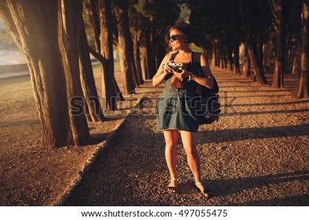 Woman with vintage camera in park alley at sunset