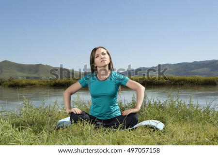 Young woman is practicing yoga at mountain river, relax in nature 