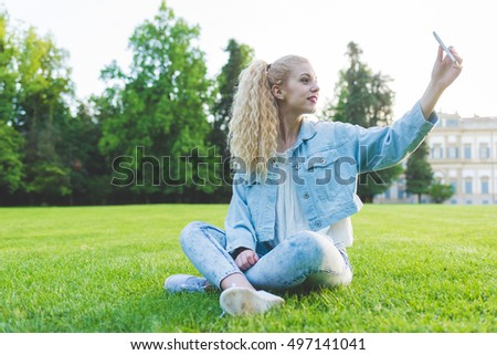 Young beautiful caucasian blonde curly hair woman taking selfie outdoor in a city park - technology, social network, communication concept