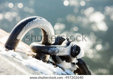 Grey metal hook with snow and blurred sea background 