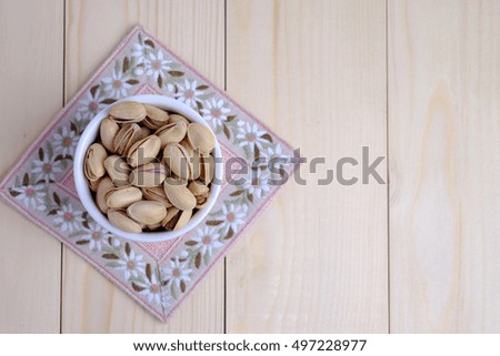 Top view of pistachio nut in cup on coaster and wooden background. Selective focus and blank space concept.