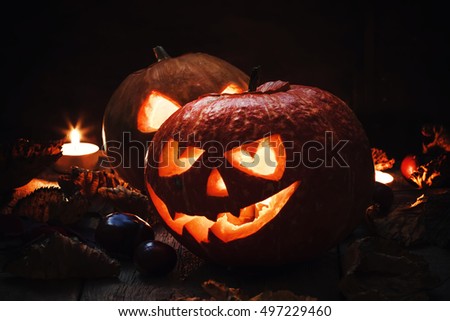 Two Halloween pumpkin Jack-o-Lantern on dark wooden background with fallen leaves and flames, selective focus