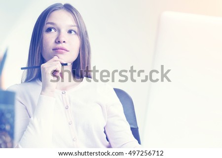 Closeup of thoughtful young woman with pencil in hand sitting at desk with laptop and office tools. Toned image