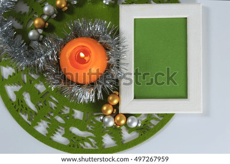 Merry Christmas and New Year greeting card on green christmas mat, silver tinsel with silver and golden christmas balls and orange candle against white background, horizontal top view