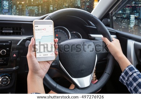 Business woman driver a touch screen of white smartphone check stock market or exchange and hand holding steering wheel in a car with night city background