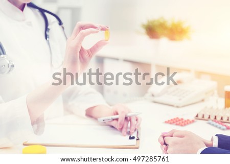 Doctor sitting at desk with patient and holding pill. Sunny day. Toned image