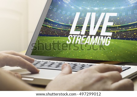 live streaming concept: man using a laptop with sports event on the screen. Screen graphics are made up.