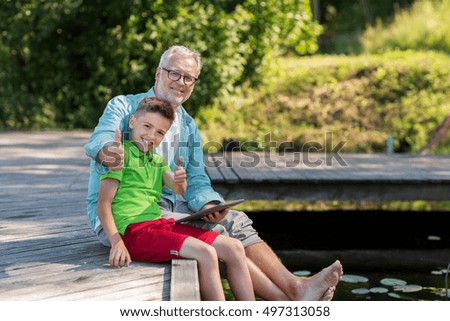 family, generation, technology, communication and people concept - grandfather and grandson with tablet pc computer sitting on river berth