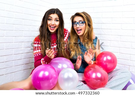 Funny positive portrait of hipster best friends girls having fun together, siting on the floor and holding a lot of pink balloons, happy party holidays time, bright clothes.