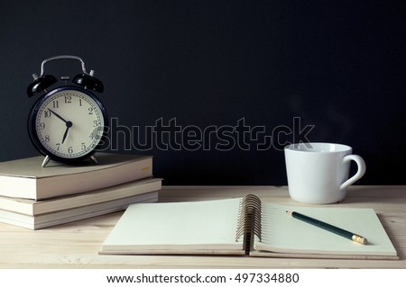 Retro alarm clock on books with notebook, pencil and cup of coffee on grunge black background on wooden table. Royalty-Free Stock Photo #497334880