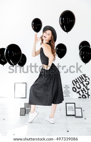 Cheerful pretty young woman standing and showing ok gesture over white background with posters and black balloons