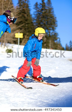 Happy school boy in colourful snowsuit learning to ski in alpine resort on sunny day during winter vacation