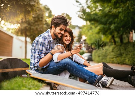 Teenage couple looking at the phone while sitting on a longboard.