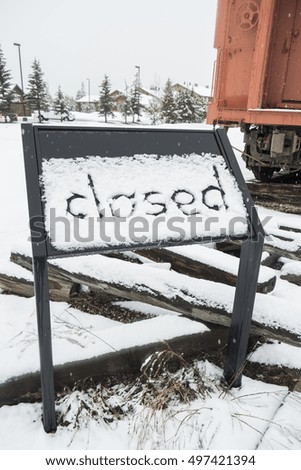 Closed sign finger made on board covered with snow next to the train railway