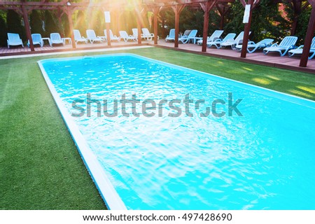 Lounge chairs near pool with sun reflected on the water 