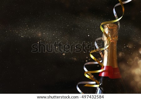 Champagne bottle in front of black background with glitter overlay. New year and celebration concept Royalty-Free Stock Photo #497432584