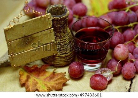 Rose grapes bunch, wicker bottle, glass with red natural organic house wine or juice, and autumn leaves on wood background. Design image with blank handmade vintage wood desk label place for text.