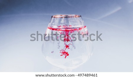 Wine glass filled with water and spreading red and yellow ink