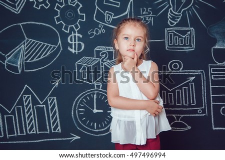 The little smart girl holding her chin on a background of wall with business or school picture