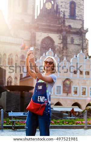 Beautiful young female traveler making self photo on her mobile phone on the background of the Church of Virgin Mary in Old Town Square in Prague. Kostel Panny Marie pred Tynem.