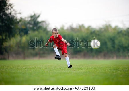 Little football player in red uniform shooting the ball
