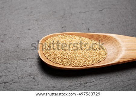 Raw white amaranth seeds in wooden spoon on black stone background. Concept of healthy and gluten free food.