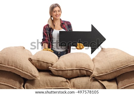 Joyful female farmer posing behind a pile of burlap sacks with an arrow pointing right isolated on white background