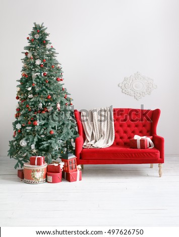 Stylish Christmas interior with an elegant red sofa. Comfort home. Armchair with fabric upholstery. Christmas tree with presents underneath in living room Royalty-Free Stock Photo #497626750